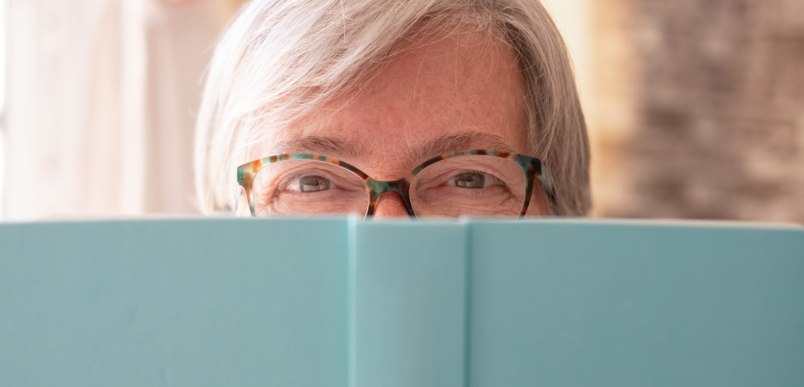 Portrait of beautiful caucasian senior woman partially hidden by a book looking at camera smiling - concept of relaxed lady enjoying retirement